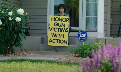 A women sitting on a porch with a sign that says: Honor Gun Victims With Action