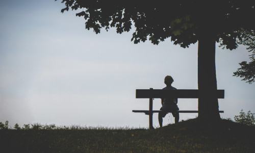 Sad kid sitting alone on a bench.