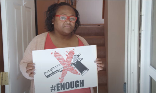 A women holding a sign with a gun on it that is Xed through and has the word ENOUGH on it.