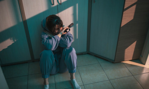 A sad and suicidal woman sitting on the floor with a gun in her hand.