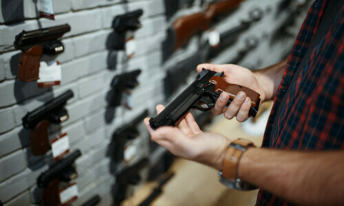 Man holding a gun with multiple guns in the background
